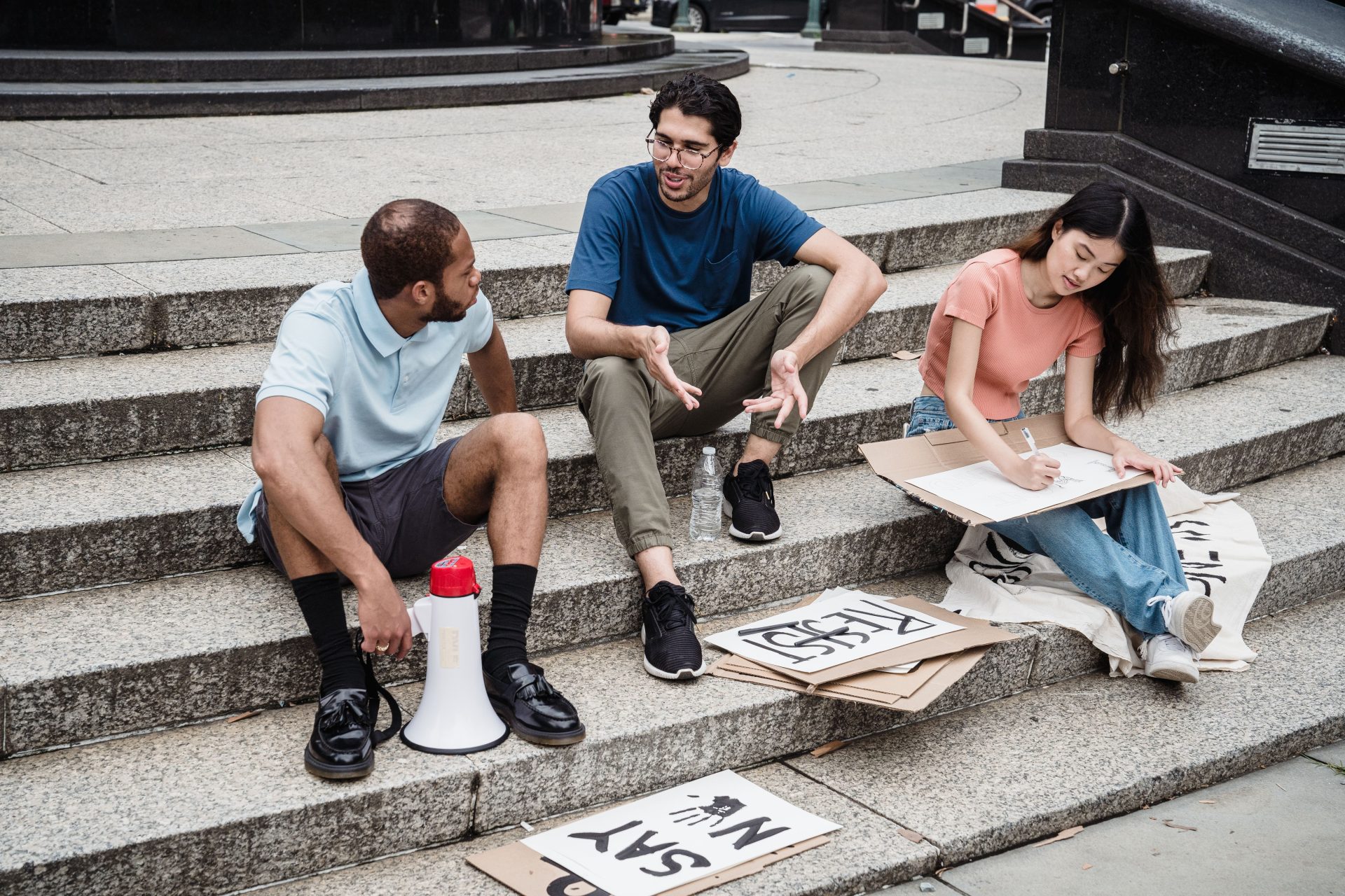 Young adults creatively brainstorming with protest signs on urban stairs.